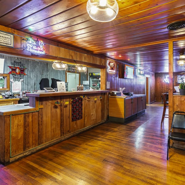 Interior of Hump's BBQ with a wooden counter, neon signs, and warm lighting.