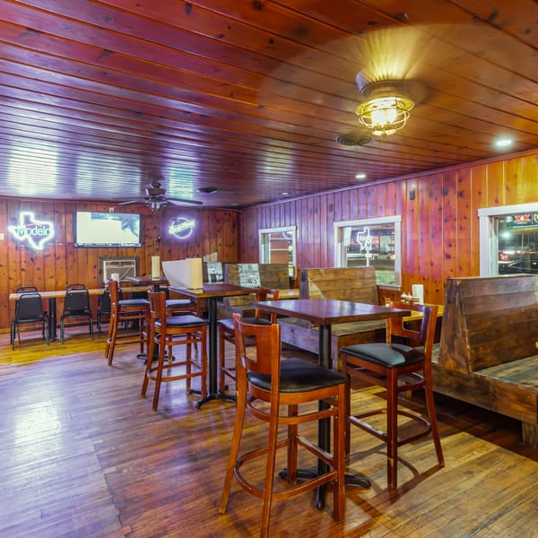 Warmly lit interior of Hump's BBQ with wooden walls, floors, tables, and benches, featuring neon signs.