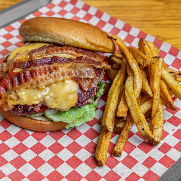 Hump's BBQ bacon cheeseburger with lettuce, tomato, and a side of seasoned fries.