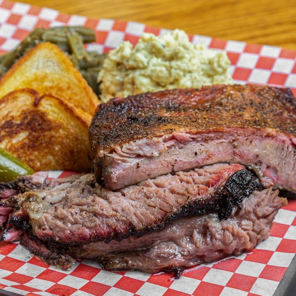 Hump's BBQ brisket with green beans, potato salad, and Texas toast on checkered paper.