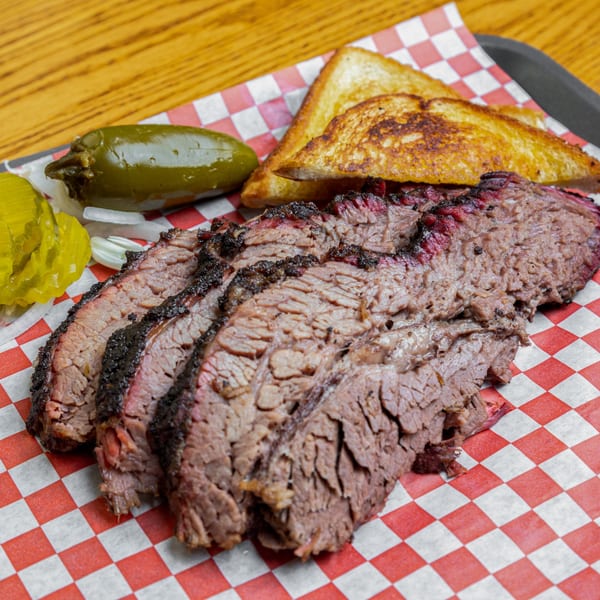 Slices of Hump's BBQ brisket with toasted bread, pickled jalapeños, and onions on checkered paper.